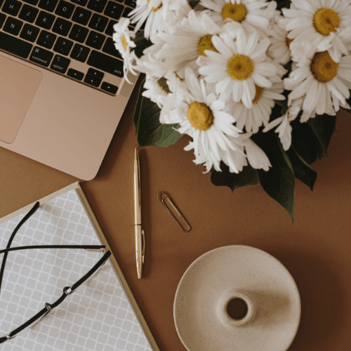 Photo vue de haut d'un bureau avec un début de clavier d'ordinateur portable, des lunettes de vue et un bouquet de paquerettes