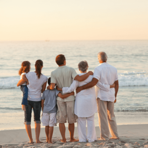 Une famille de dos devant la mer sur une plage au coucher du soleil
