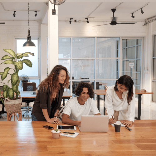 Groupe de 3 personnes souriantes dans une salle de réunion devant un ordinateur portable